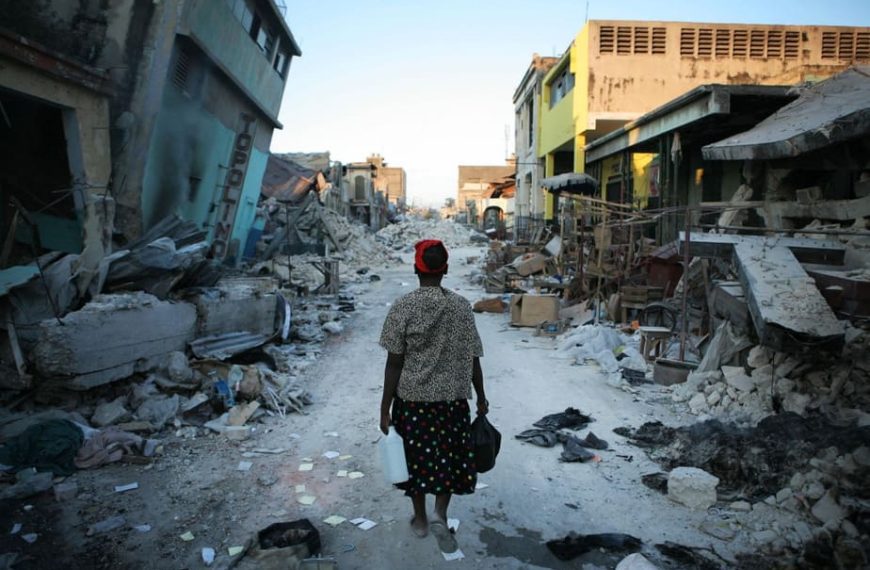 Une femme agée marchant au milieu des décombres.